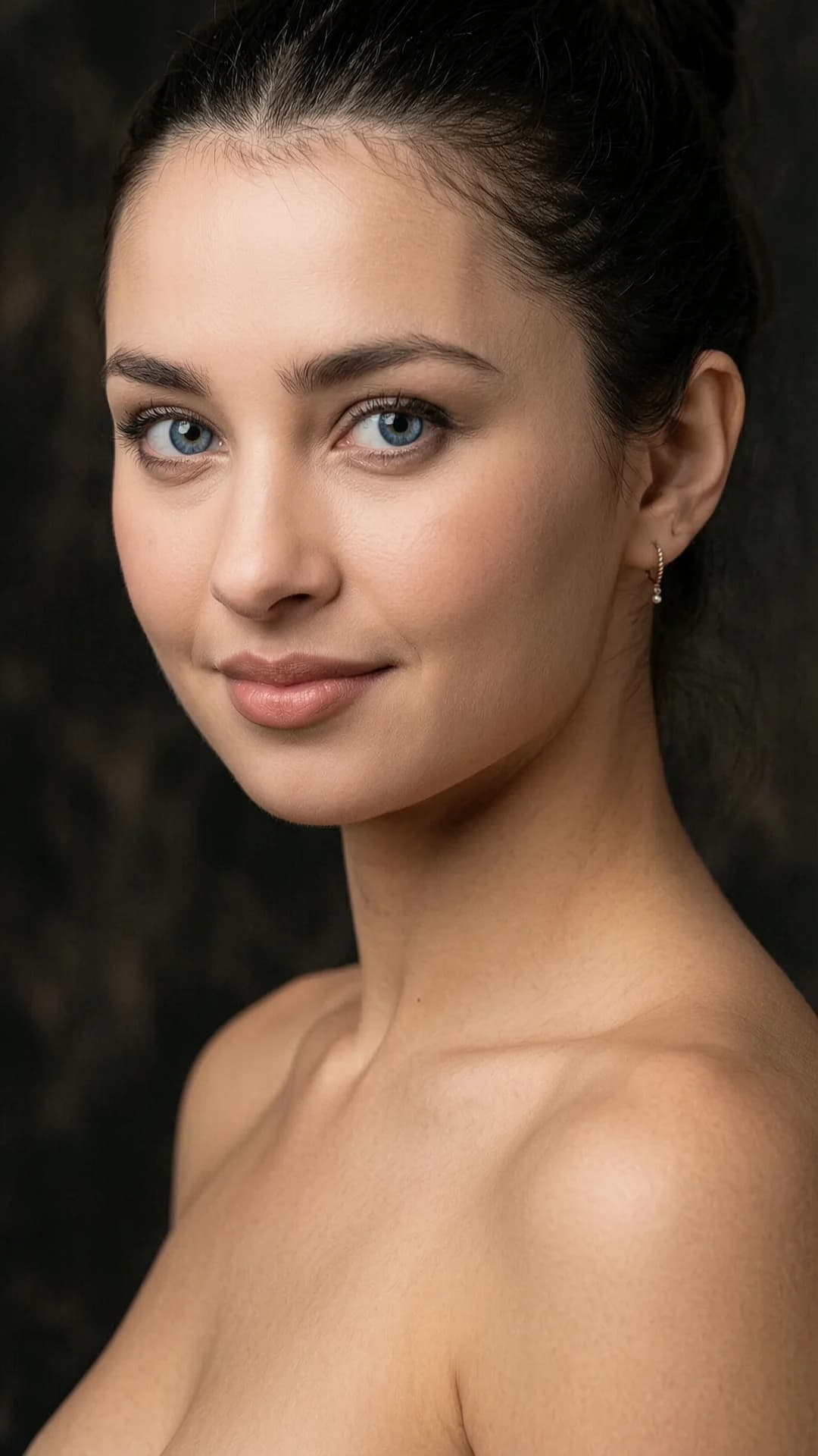 A 26-year-old Latina woman with fair skin of soft natural texture, long brunette hair pulled back, striking blue eyes with clear reflections, delicate facial features, and a fit body type, captured in a close-up portrait from shoulders up with classic composition, camera positioned at or slightly above eye level for strong subject separation against a dark blurred background with shallow depth of field, her face slightly turned left while maintaining direct eye contact with a gentle and calm expression conveying an elegant and quiet aura, wearing a small delicate earring, illuminated by soft studio lighting with key light from the upper-left creating natural highlights and soft shadows in warm-neutral tones, realistic skin texture with subtle sheen, professional photography style, 8K ultra-detailed realism, cinematic subtle grading, natural colors, photo-realistic. Flawless anatomy, no extra digits, no extra limbs, realistic skin texture, high-detail.