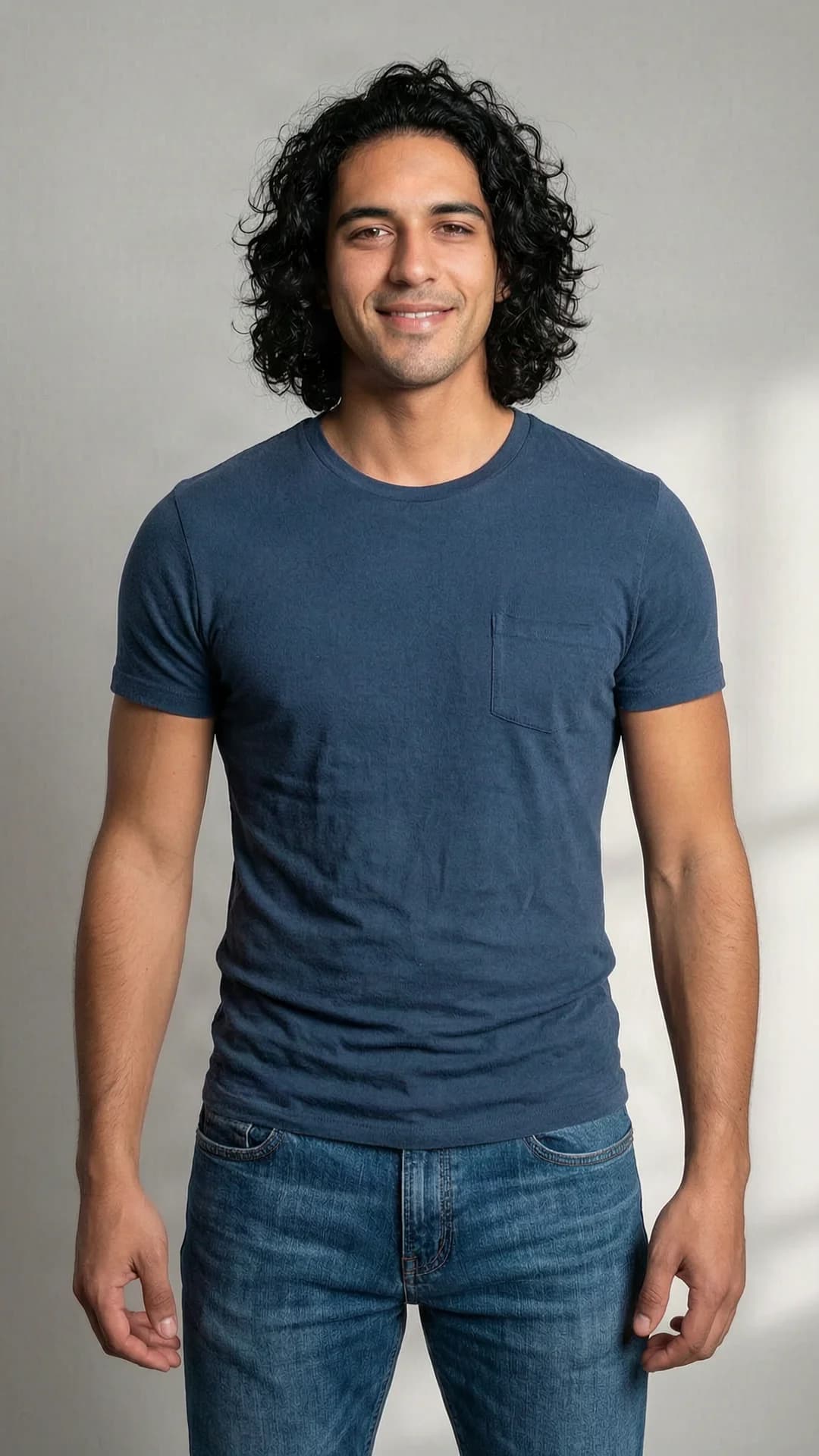 30-year-old muscular Latino man with curly black hair and brown eyes, wearing fitted jeans and a stylish t-shirt in a casual look, standing in a relaxed pose for a portrait picture, medium close-up from front angle with direct view, intense direct eye contact with a warm friendly smile and lips curved upward, soft natural lighting highlighting defined muscles and casual attire, realistic style, Flawless anatomy, no extra digits, no extra limbs, realistic skin texture, high-detail.